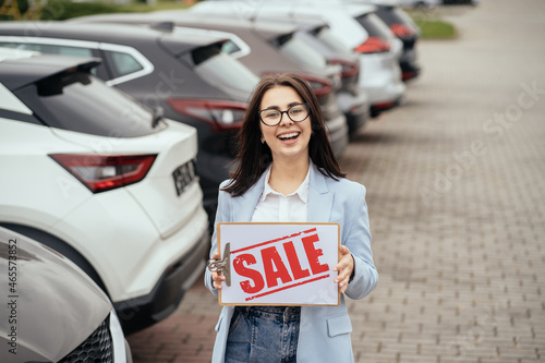 Woman standing near row of new cars with sale banner