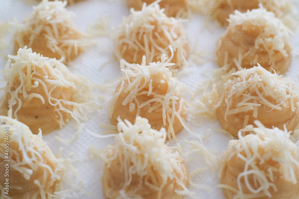 Uncooked French gougères with grated cheese on top, while preparing to put in oven. It's a traditional pastry made with savory choux dough. Uncooked French gougères with grated cheese on top, while preparing to put in oven. It's a traditional pastry made with savory choux dough.