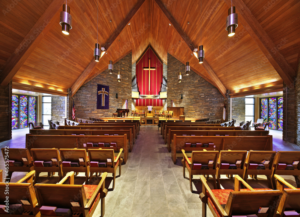 Interior of beautiful church with stonework, wood ceiling, stained glass windows, organ, and pews
