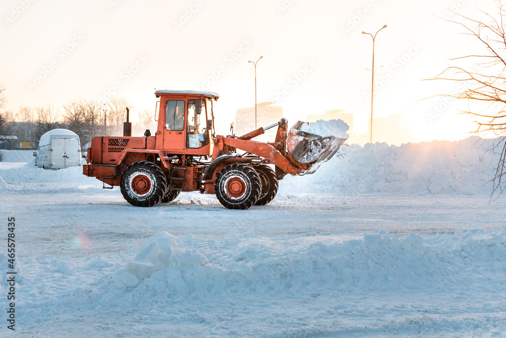 A bulldozer removes snow with a bucket after a blizzard. Cleaning snow drifts with a bulldozer. The consequences of a snow storm. A bulldozer removes snow with a bucket after a blizzard. Cleaning snow drifts with a bulldozer. The consequences of a snow storm.