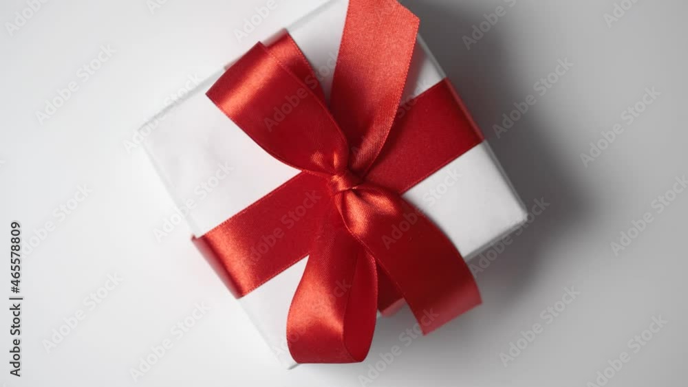 Rotate white gift box with red ribbon on white background with place for your text. Video motion on Valentines Day, mothers day or Birthday. Top view 4k footage Rotate white gift box with red ribbon on white background with place for your text. Video motion on Valentines Day, mothers day or Birthday. Top view 4k footage