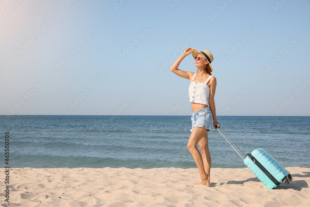 Beautiful woman with suitcase on sandy beach near sea