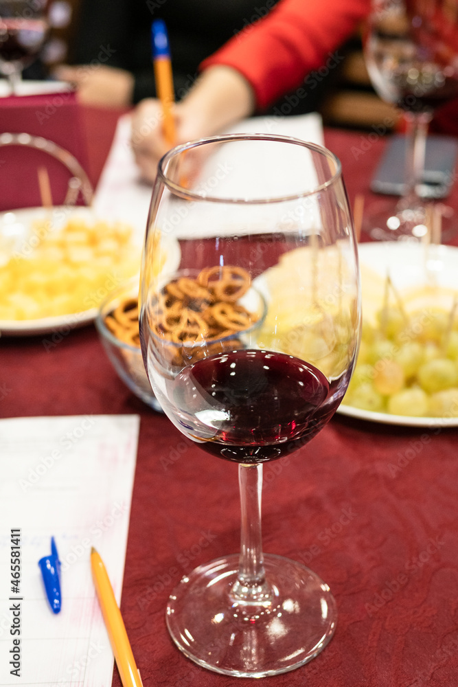 Naklejka premium red grape wine tasting - wineglass with portion on tested wine on table