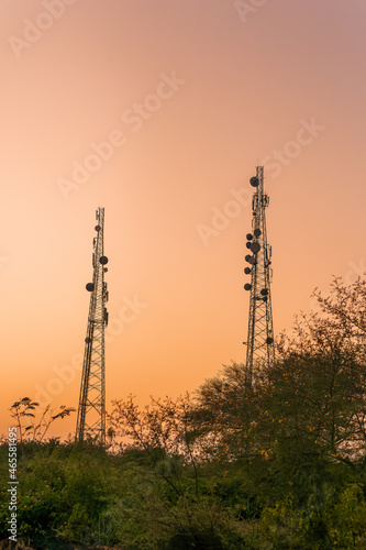 Sunset view of two telecom towers with tree and bushes in the foreground