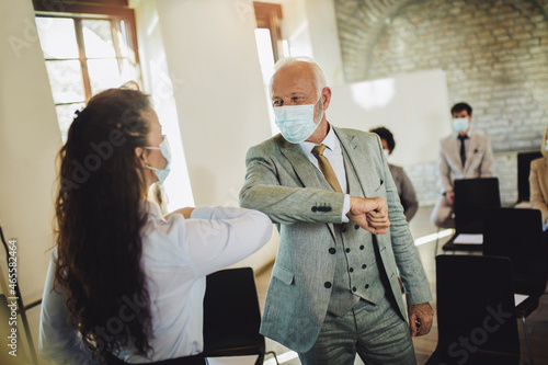 Business man and woman with safety masks greeting with elbow bump in office. Virus protection concept photo