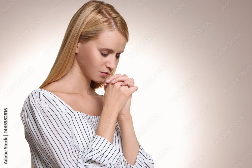 Religious young woman with clasped hands praying against light background. Space for text Religious young woman with clasped hands praying against light background. Space for text