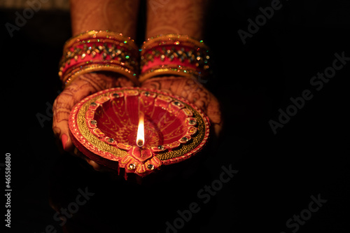 Beautiful Woman lady hand with bangles holding Eco Friendly Glowing Clay Diya Deep Dia lamps for Hindu festival Laxmi pooja or puja Diwali on a blck background