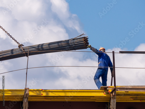 A worker holds a bundle of reinforcing bars while unloading. Lifting reinforcing bars on a building under construction. Reinforcement of concrete structures. Reinforced concrete production photo