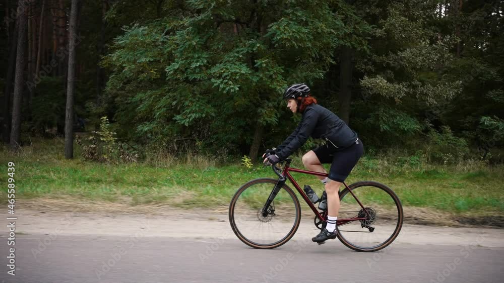 Professional woman biker training in forest, riding uphill on bicycle, preparing for competitions, tracking shot Professional woman biker training in forest, riding uphill on bicycle, preparing for competitions, tracking shot