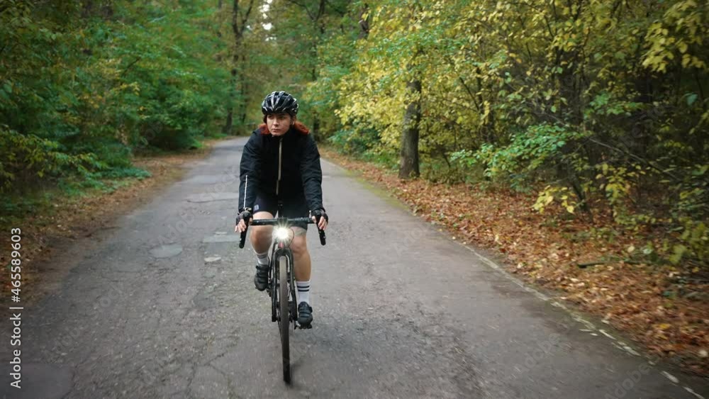 Active leisure. Follow shot of young sporty woman cyclist wearing protective helmet riding alone in green autumn forest Active leisure. Follow shot of young sporty woman cyclist wearing protective helmet riding alone in green autumn forest