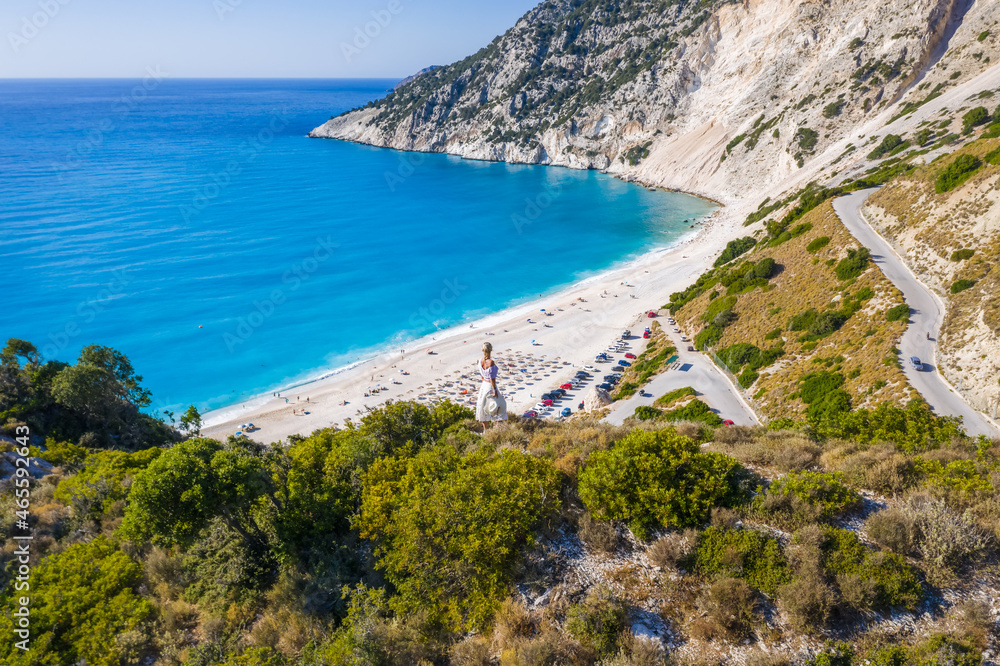 Obraz premium Happy woman standing on top of a rock with hat enjoying Myrtos Beach. Cephalonia island, Greece