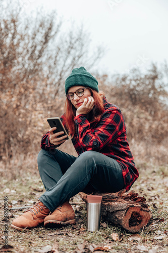 Happy girl tourist woman uses smartphone, resting near camping on nature in autumn season photo
