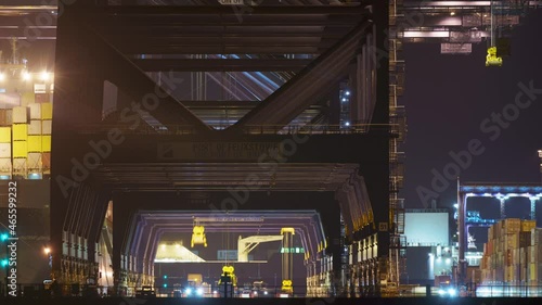 Felixstowe, United Kingdom - October 24 2021: A timelapse of containers being lifted from port vehicles to be loaded onto a ship, which can be seen at the edge of the frame. photo
