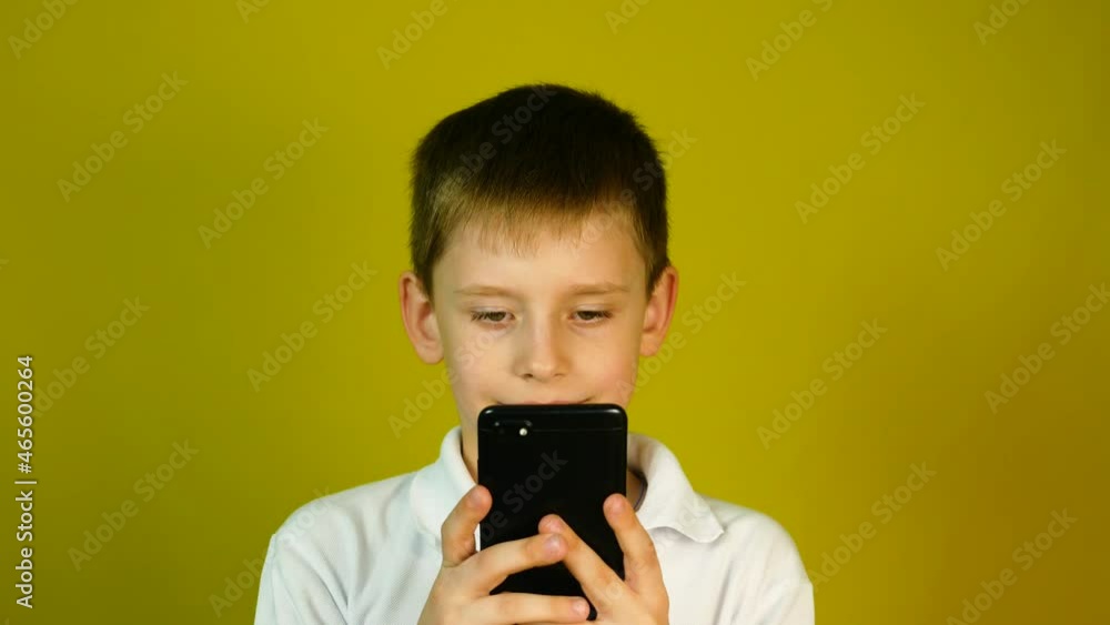 Portrait of a Caucasian boy 7-9 years old in studio shooting on a yellow background holding a smartphone. The child uses a gadget while holding in his hands. Boy with a phone in his hands Portrait of a Caucasian boy 7-9 years old in studio shooting on a yellow background holding a smartphone. The child uses a gadget while holding in his hands. Boy with a phone in his hands