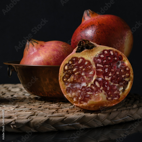 Some pomegranate fruits before a black background. Red pomegranate opened and seeds over the cutting board © Julian