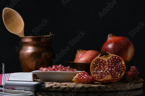 Some pomegranate fruits before a black background. Red pomegranate opened and seeds over the cutting board © Julian