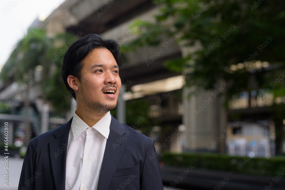 Portrait of Asian businessman outdoors in the city smiling and thinking Portrait of Asian businessman outdoors in the city smiling and thinking
