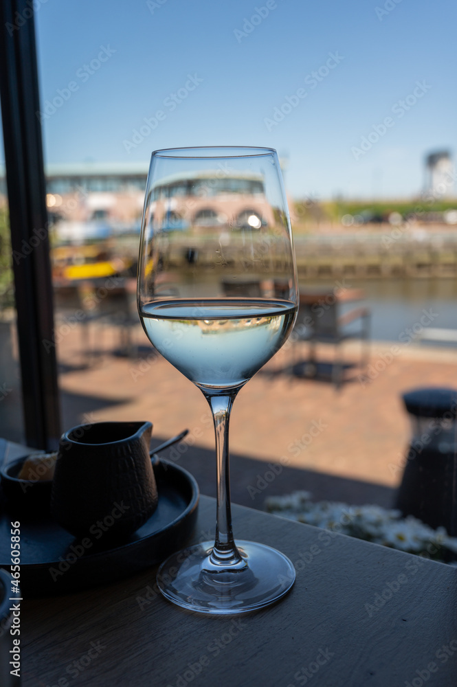 Glass of white wine served in cafe with view on harbour of Harlingen, vacation in Friesland, Netherlands Glass of white wine served in cafe with view on harbour of Harlingen, vacation in Friesland, Netherlands