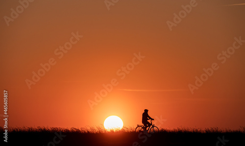 Silhouette of man on bike on grass on sunset with back lite and sun on backgound