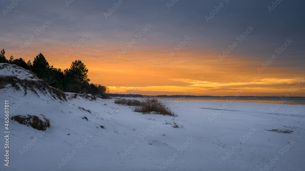Bright orange winter sunset over the sea, beach covered with snow