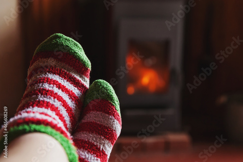 Feet legs in winter clothes wool socks at fireplace background. Woman sitting at home on winter or autumn evening relaxing and warming up. Winter and cold weather concept. Hygge Christmas eve.