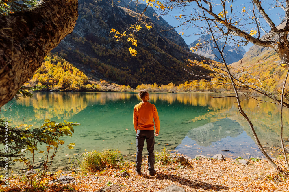 Traveller look at crystal lake in autumnal mountains. Mountain lake and hiker man