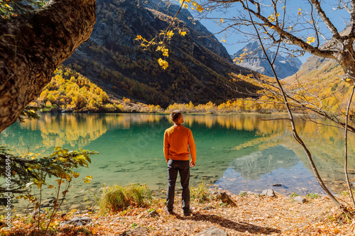 Traveller look at crystal lake in autumnal mountains. Mountain lake and hiker man