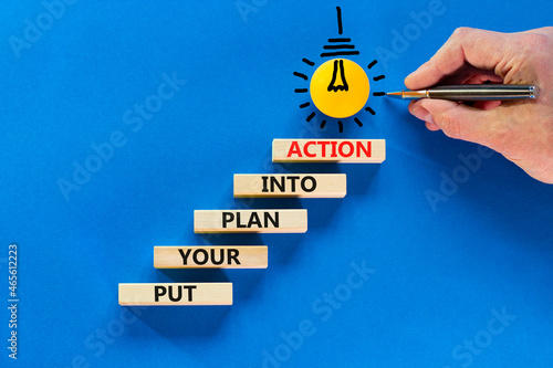 Put your plan into action symbol. Wooden blocks with words Put your plan into action. Light bulb icon. Businessman hand, pen. Blue background, copy space. Business, plan into action concept.