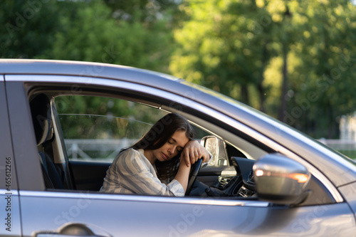 Frustrated female sit in car leaning on steering wheel tired with closed eyes. Woman mother of middle age exhausted with problems in family with kids or at work stay at parking doesn't want to go home