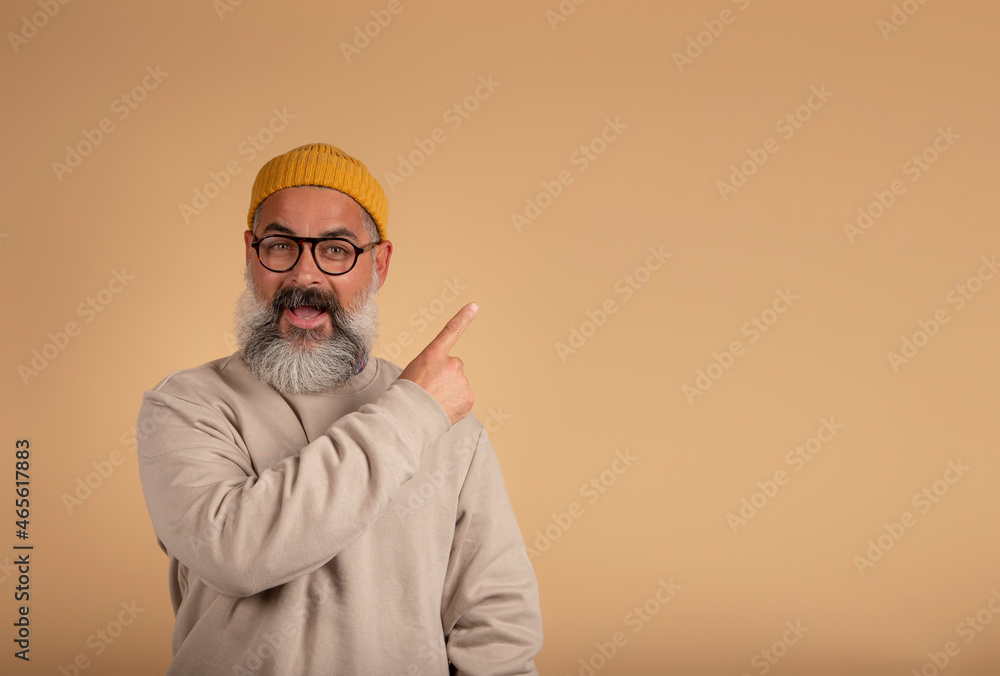 Emotional photo of a dejected bearded man opens his mouth wide, looks at the camera and points in the free space, says: Wow, that's something incredible! People and emotions concept