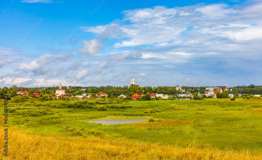 Summer landscape with buildings, churches, trees, shrubs, grass, sky with clouds of the city of Suzdal in Russia
