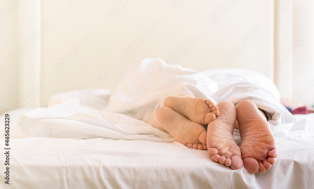 A pair of bare feet under the covers in the bedroom in the morning sun A pair of bare feet under the covers in the bedroom in the morning sun