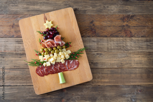 Christmas tree shaped cheese and charcuterie board with wooden background. Top view. Copy space.