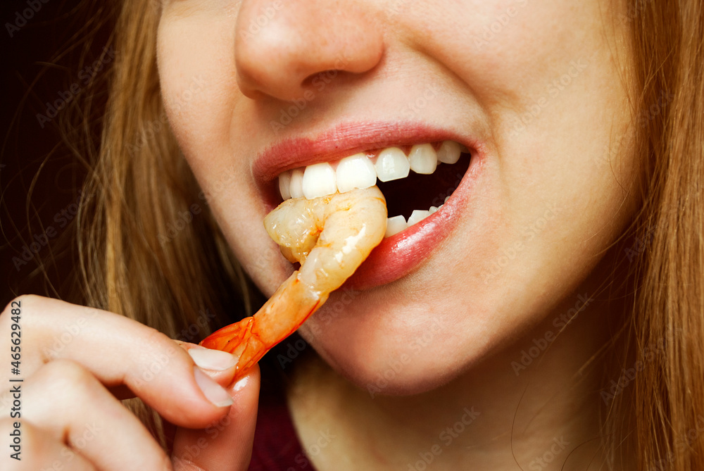 A woman with her hands eats a large appetizing shrimp. Selective focus. Mouth bites shrimp, close-up. A woman with her hands eats a large appetizing shrimp. Selective focus. Mouth bites shrimp, close-up.