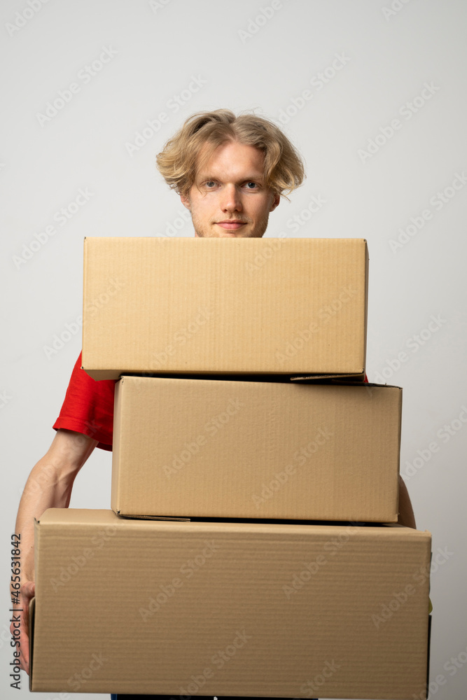 Cheerful delivery man. Happy young courier holding a cardboard boxes and smiling while standing against white background. Delivery man holding pile of cardboard boxes in front of himself. Cheerful delivery man. Happy young courier holding a cardboard boxes and smiling while standing against white background. Delivery man holding pile of cardboard boxes in front of himself.