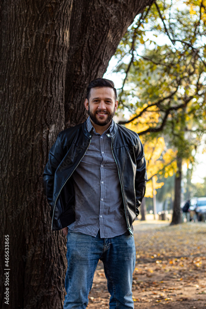happy white man in a park by a tree and using a leather jacket happy white man in a park by a tree and using a leather jacket
