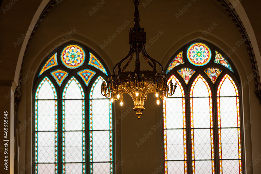 A beautiful chandelier in a church with two huge stained glass windows in the background