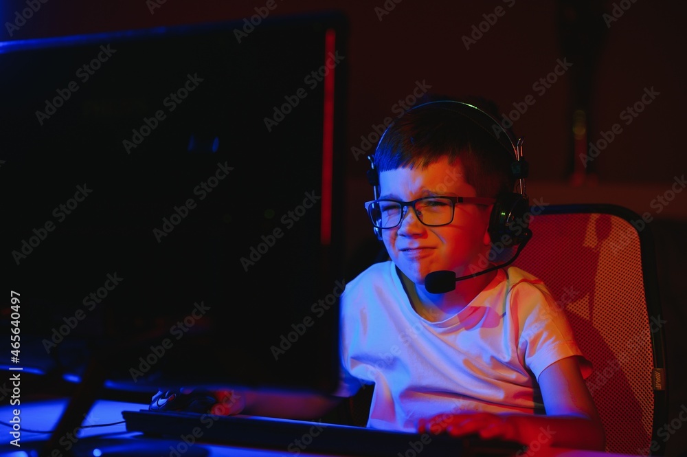 Child online broadcasts computer game, boy streams in headphones on rgb lighting background Child online broadcasts computer game, boy streams in headphones on rgb lighting background