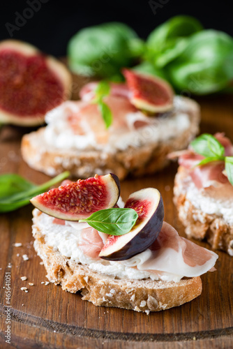 Toast bruschetta with ricotta, figs, ham on wooden serving board, closeup view. Gourmet snack