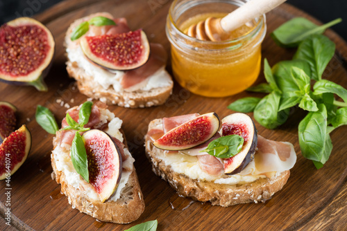 Fig and prosciutto bruschetta served with basil and honey on a wooden board, closeup view. Italian appetizer food