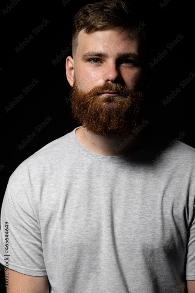 Fototapeta premium Portrait of handsome serious unshaven guy with long beard and handlebar moustache in grey t-shirt looking forward.