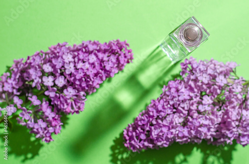 Purple lilac flowers and a glass bottle with perfume on a green background. Bright shadows and light. Place for your text. Flat lay.