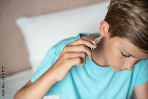 Teen boy with otitis and earaches holding drops for treatment. Kid suffering from otitis. Acute ear pain, inflammatory disease of the middle ear