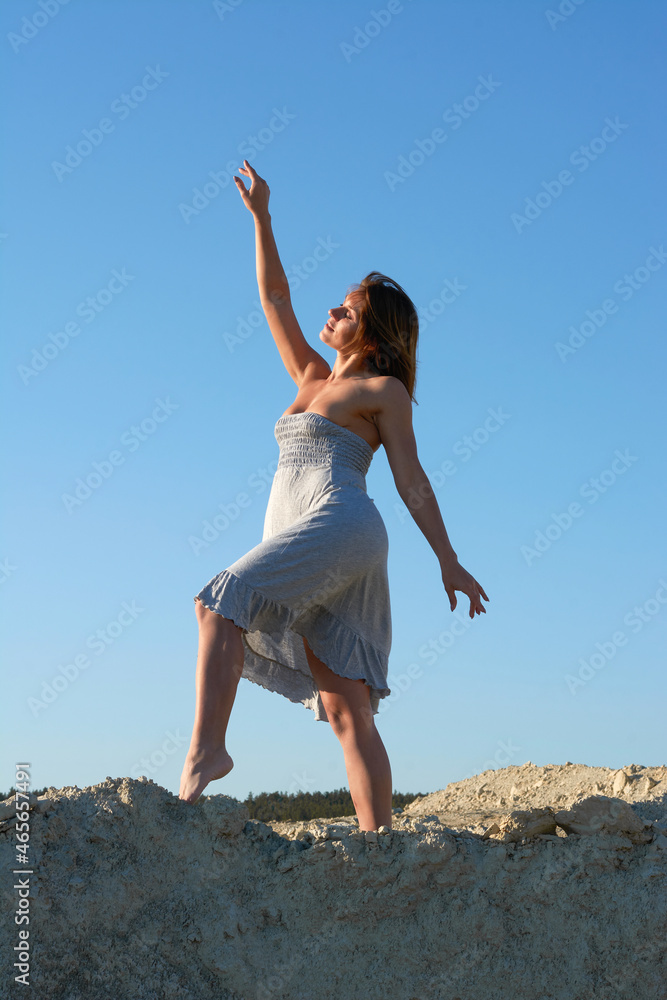 beautiful brunette girl dancing and looking at the sun.girl in a white dress in the desert against the blue sky. beautiful brunette girl dancing and looking at the sun.girl in a white dress in the desert against the blue sky.