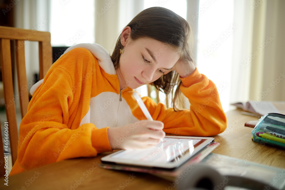 Preteen schoolgirl doing her homework with digital tablet at home. Child using gadgets to study. Education and distance learning for kids. Homeschooling during quarantine. Preteen schoolgirl doing her homework with digital tablet at home. Child using gadgets to study. Education and distance learning for kids. Homeschooling during quarantine.