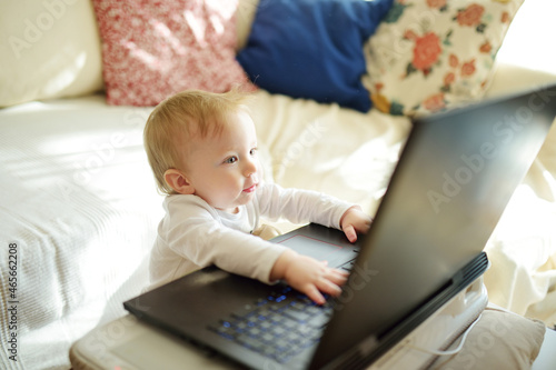 Little IT guy. Cute little baby holding hands on laptop keyboard and looking at monitor while sitting on the bed