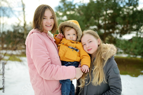 Two big sisters and their baby brother having fun outdoors. Two young girls holding their baby boy sibling on winter day. Kids with large age gap. © MNStudio
