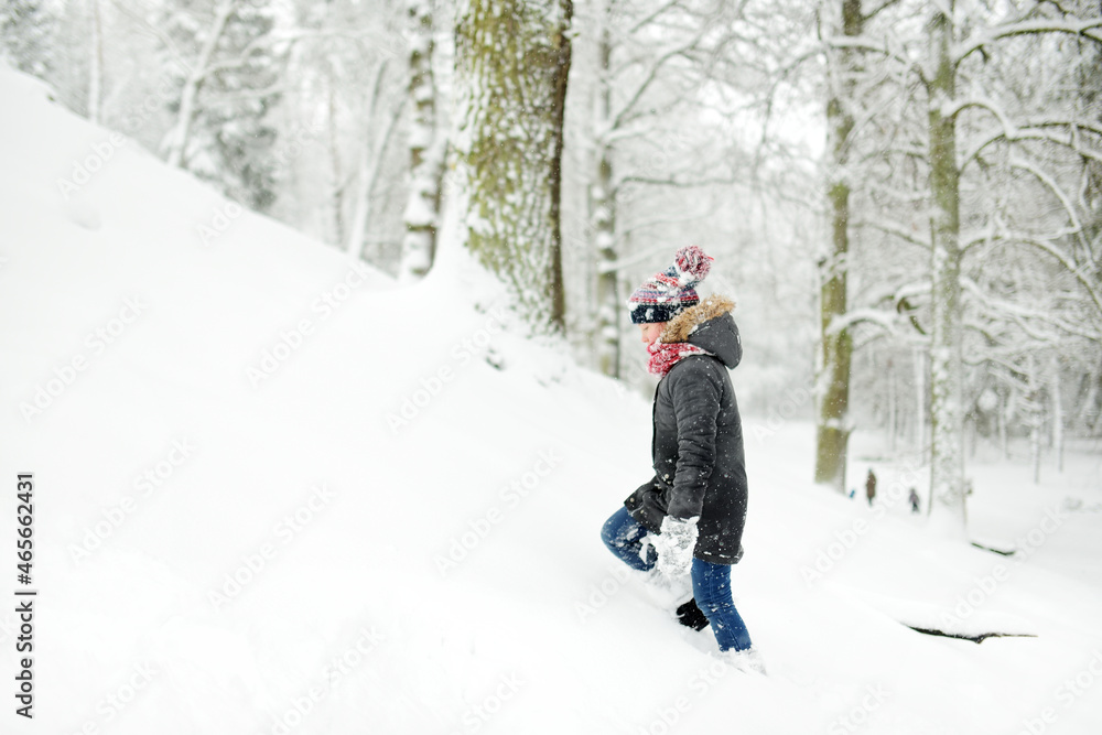 Adorable girl having fun in beautiful winter park during snowfall. Cute child playing in a snow. Winter activities for family with kids.