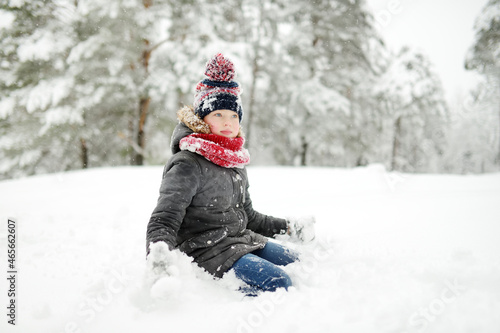 Adorable girl having fun in beautiful winter park during snowfall. Cute child playing in a snow. Winter activities for family with kids.