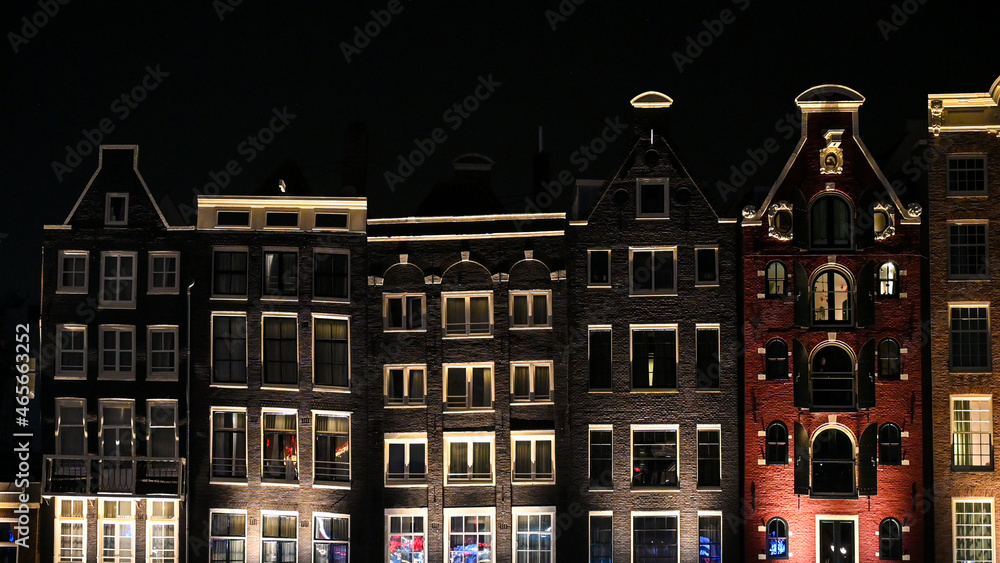 Famous houses in city of Amsterdam at night. Typical Dutch houses with colorful facades. Dancing houses and river canal in Netherland.